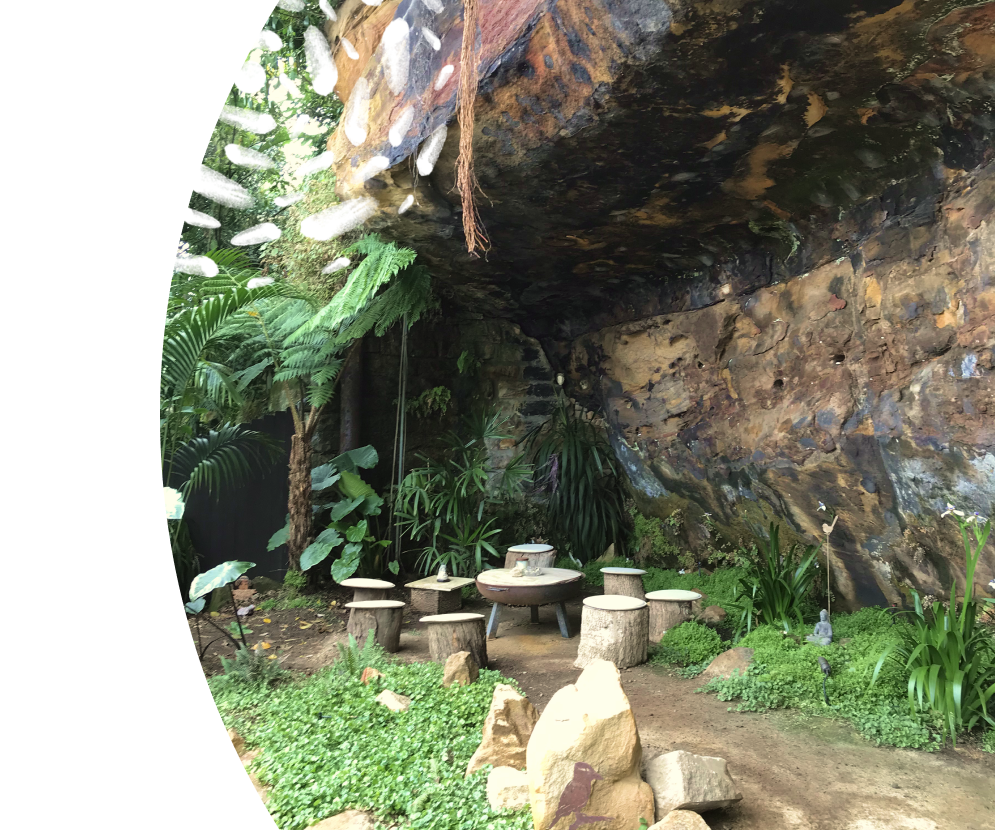 'Robyn's Nest' a gathering place at the base of a cliff, with a set of wooden log stools seated around a firepit in a circle.