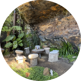 'Robyn's Nest' a gathering place at the base of a cliff, with a set of wooden log stools seated around a firepit in a circle.
