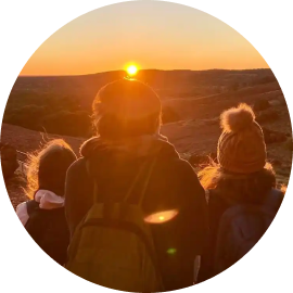 A group of people walking through the desert at sunset